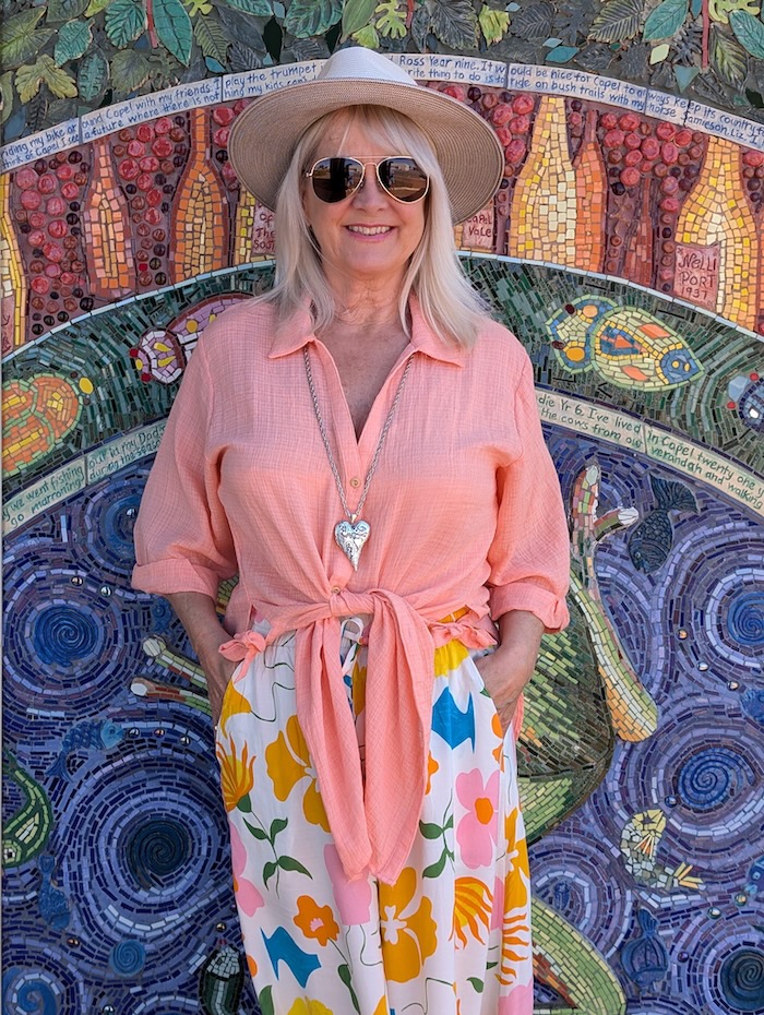 Floral boho style wide leg pants worn with peach colored shirt and hat to create a summery bohemian look.