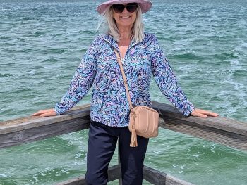 Woman wearing sun protective clothing; a UPF50 top, a wide brimmed sun hat and navy blue pants.