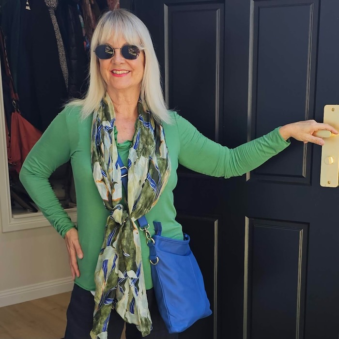 Woman wearing a green top, silk scarf and leather handbag.