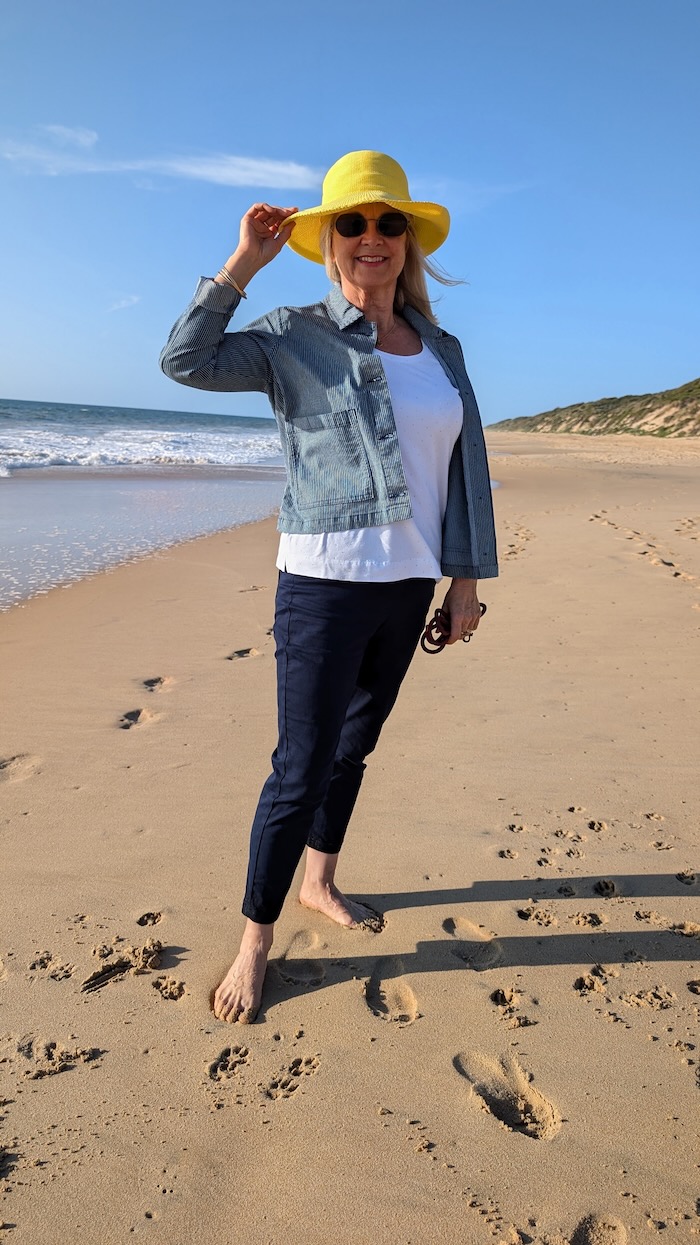 Woman on a beach wearing a bright yellow sun hat, and a lightweight travel outfit.